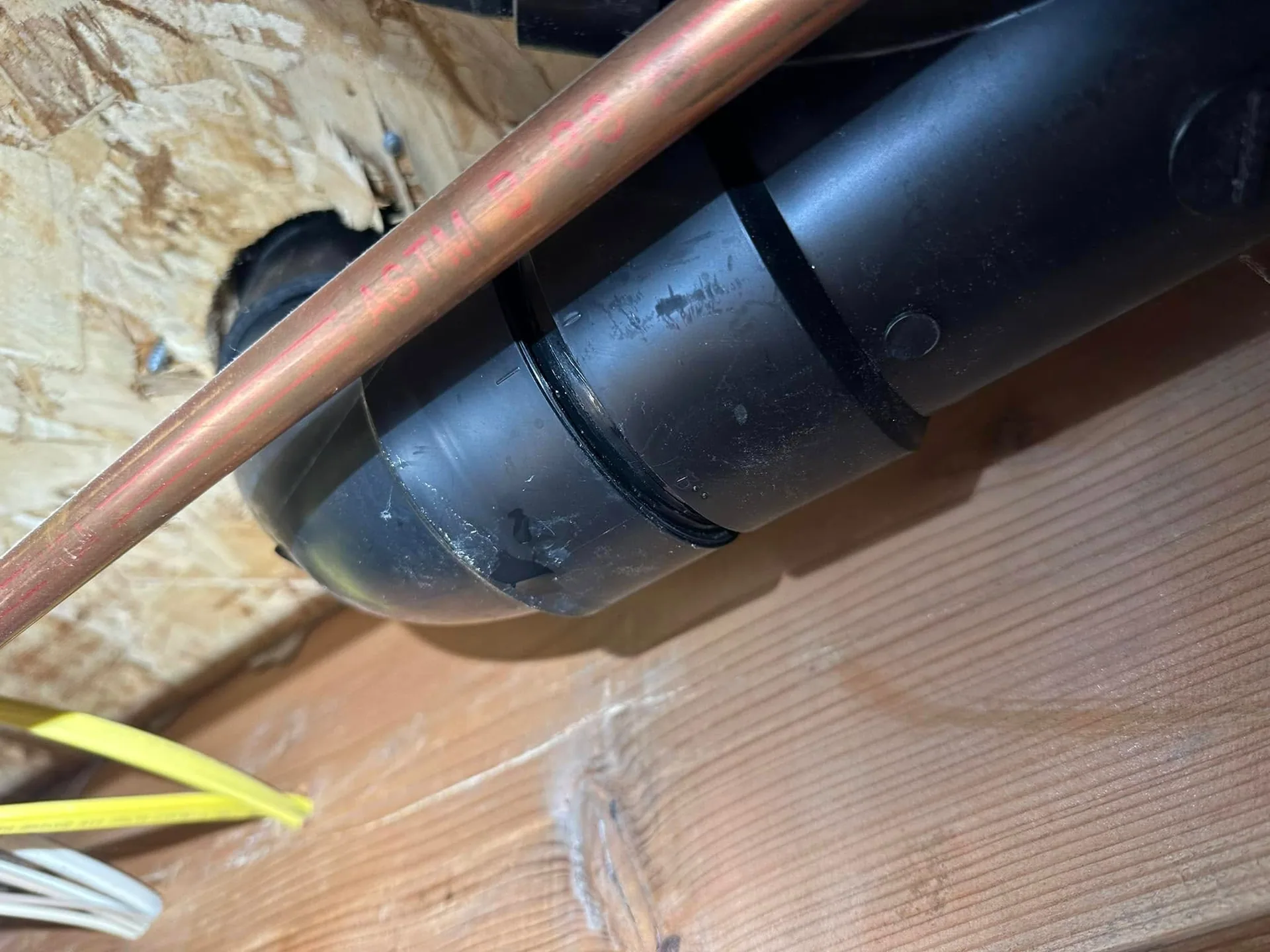 Black abs drain elbow copper pipe floor joist closeup