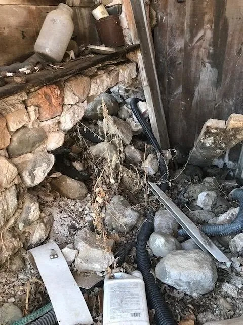 Crumbling fieldstone foundation wall loose rocks debris corrugated pipe