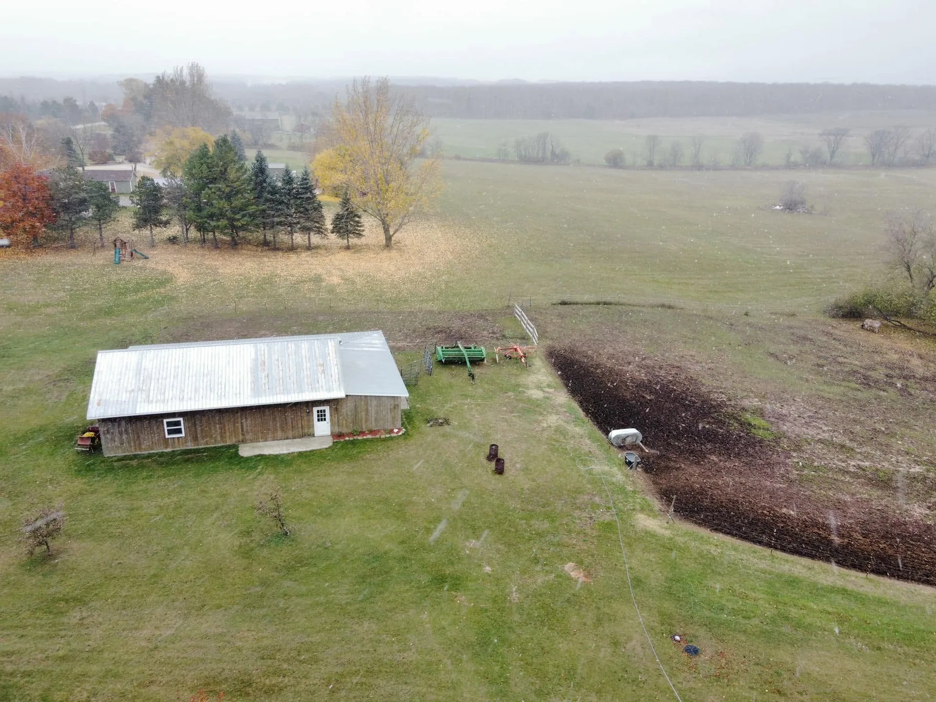 Drone aerial wood pole barn metal roof tilled garden plot snow flurries